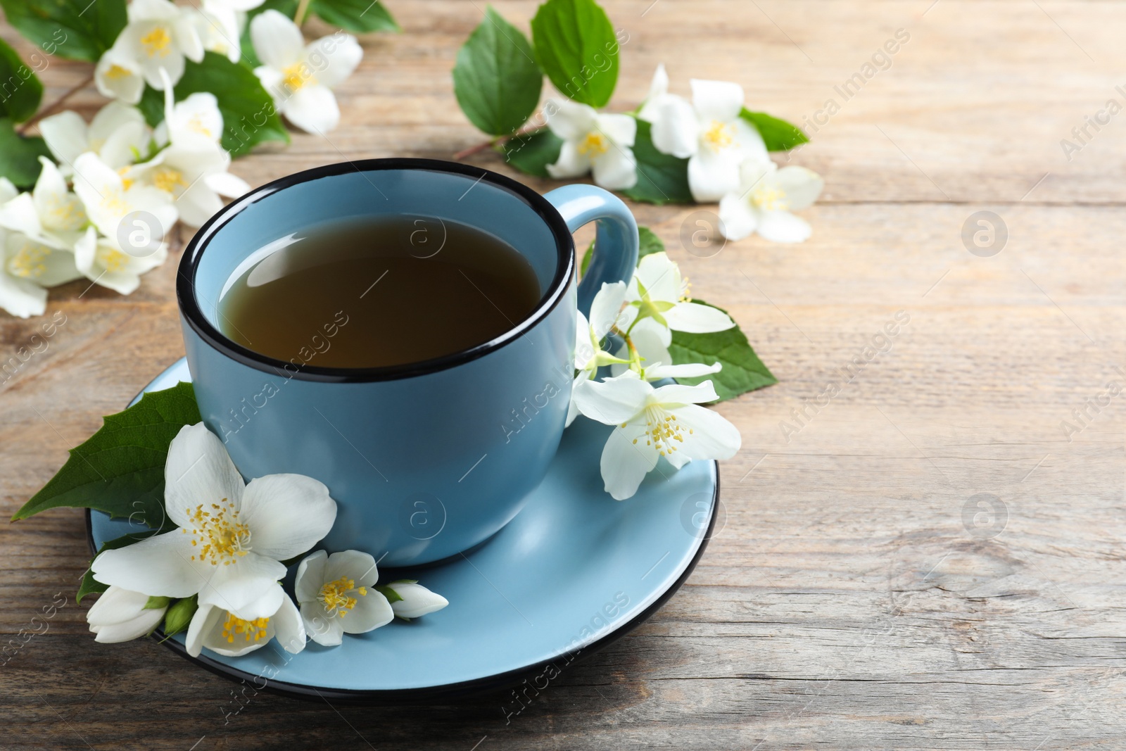 Photo of Cup of tea and fresh jasmine flowers on wooden table