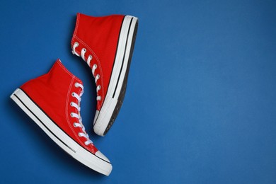 Photo of Pair of new stylish red sneakers on blue background, flat lay. Space for text