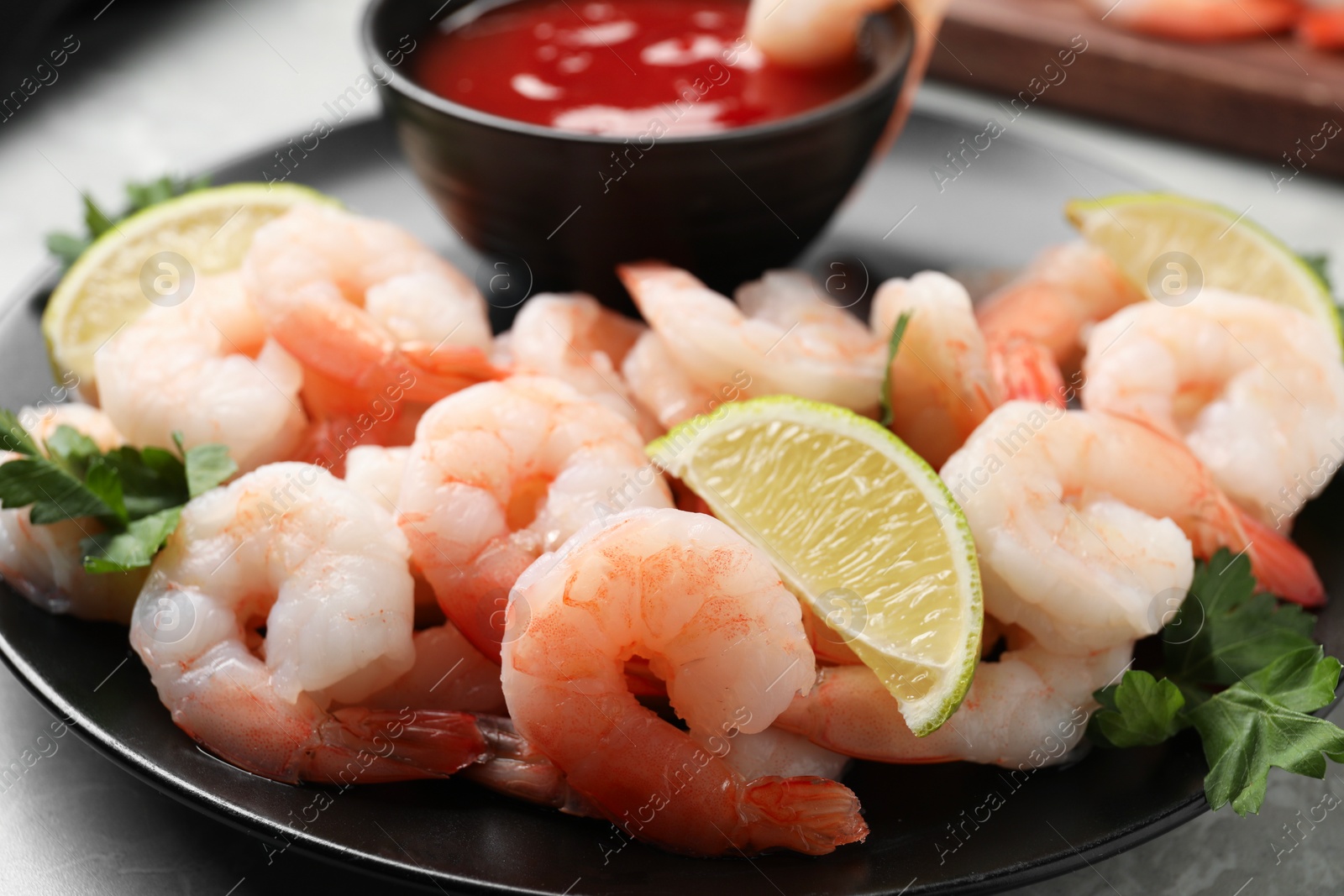 Photo of Tasty boiled shrimps with cocktail sauce, parsley and lime on light grey table, closeup