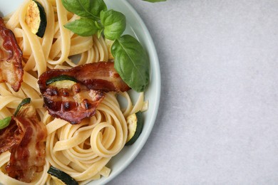 Photo of Tasty pasta with bacon and basil on light grey table, top view. Space for text