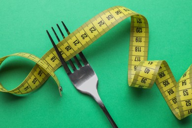 Fork with measuring tape on green background, top view. Diet concept