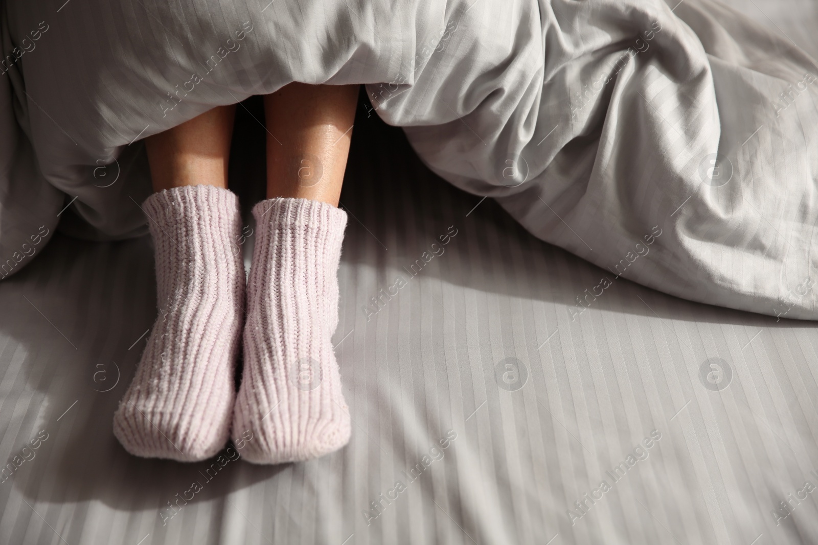 Photo of Woman wearing knitted socks under blanket in bed, closeup