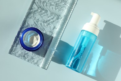 Bottle and jar of cosmetic products on light blue background, flat lay