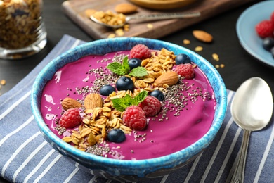 Photo of Delicious acai smoothie with granola and berries in dessert bowl on table