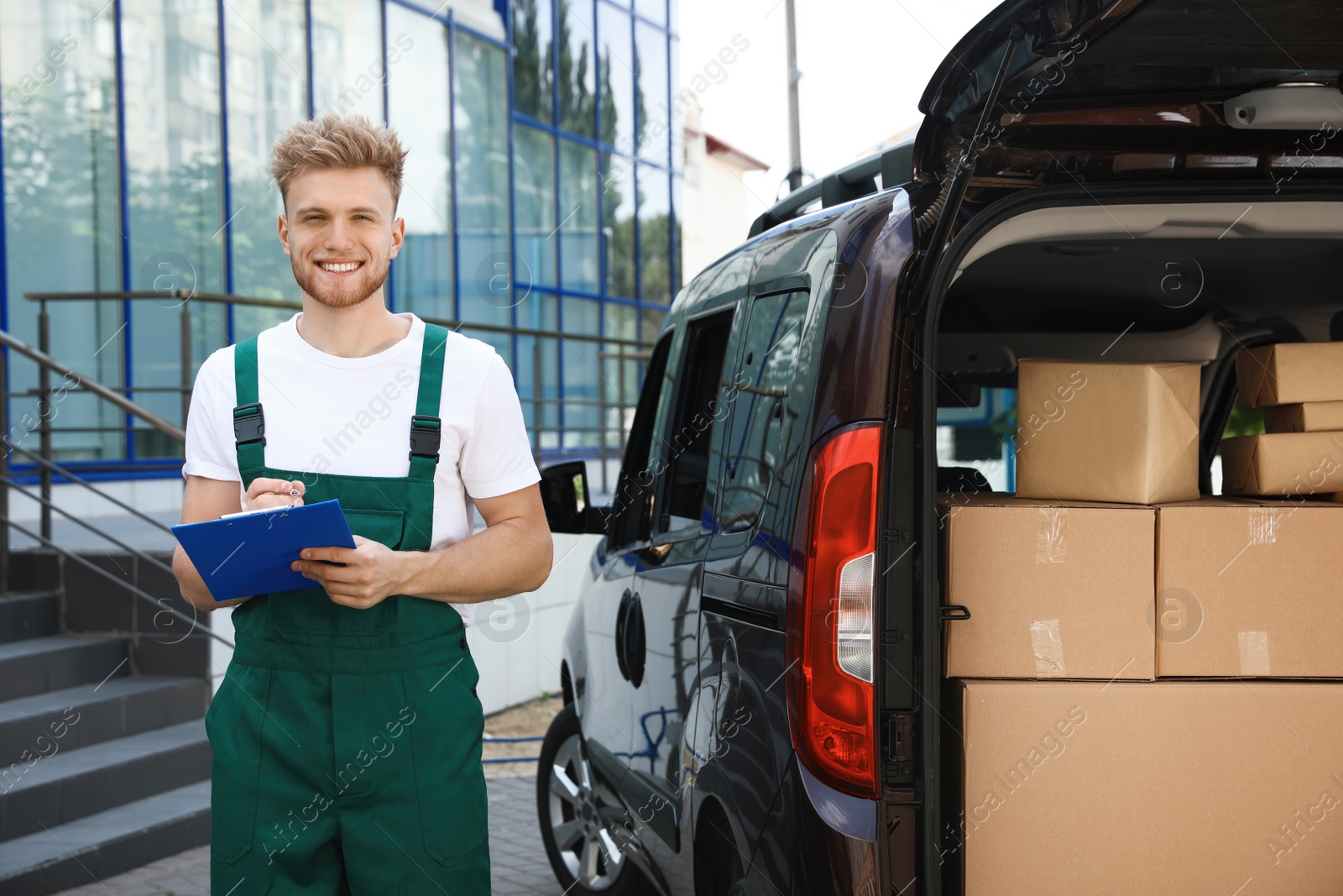 Photo of Young courier holding clipboard near delivery van with parcels outdoors