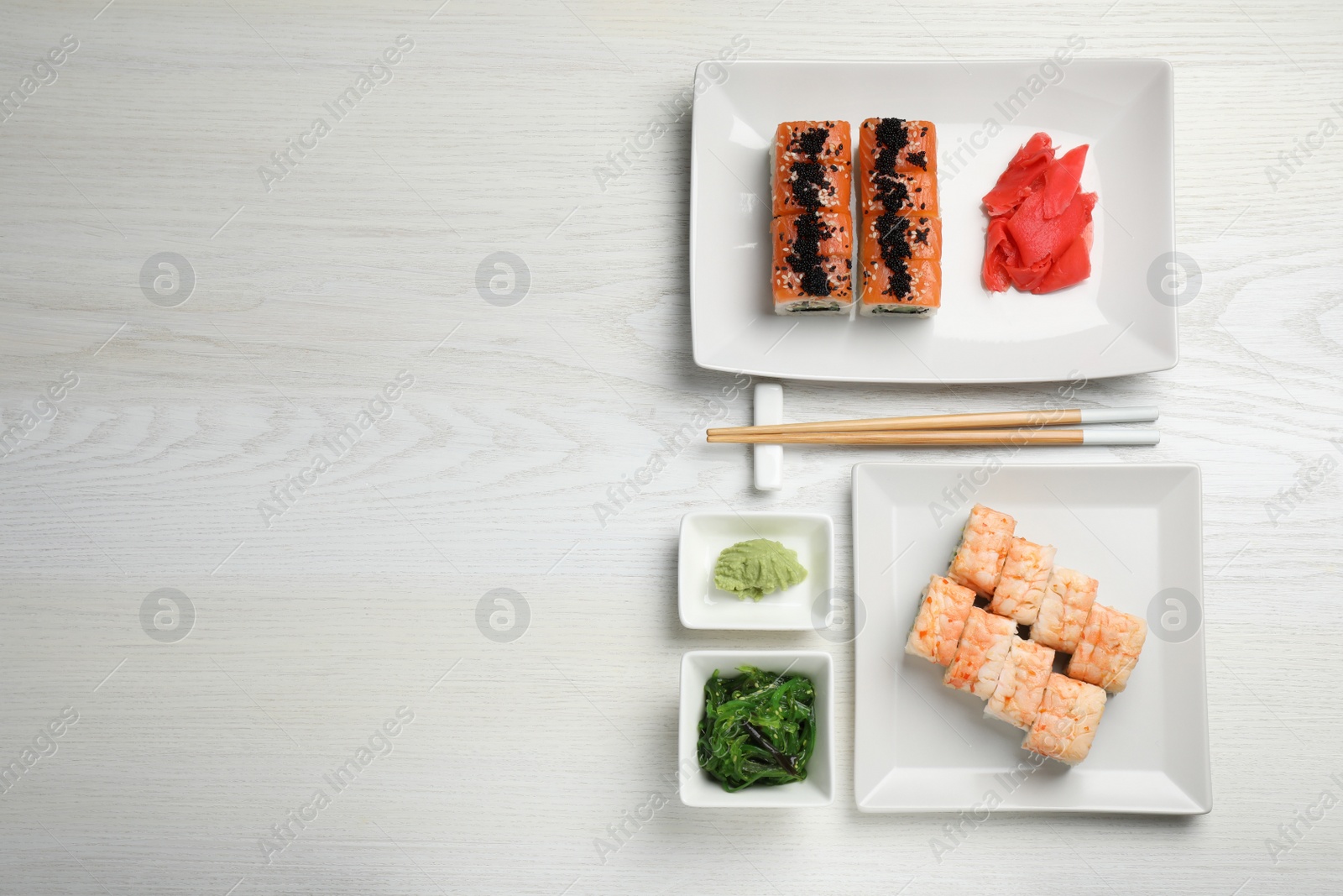 Photo of Delicious sushi rolls served on white wooden table, flat lay. Space for text