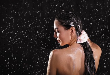 Photo of Young woman washing hair on black background. Space for text
