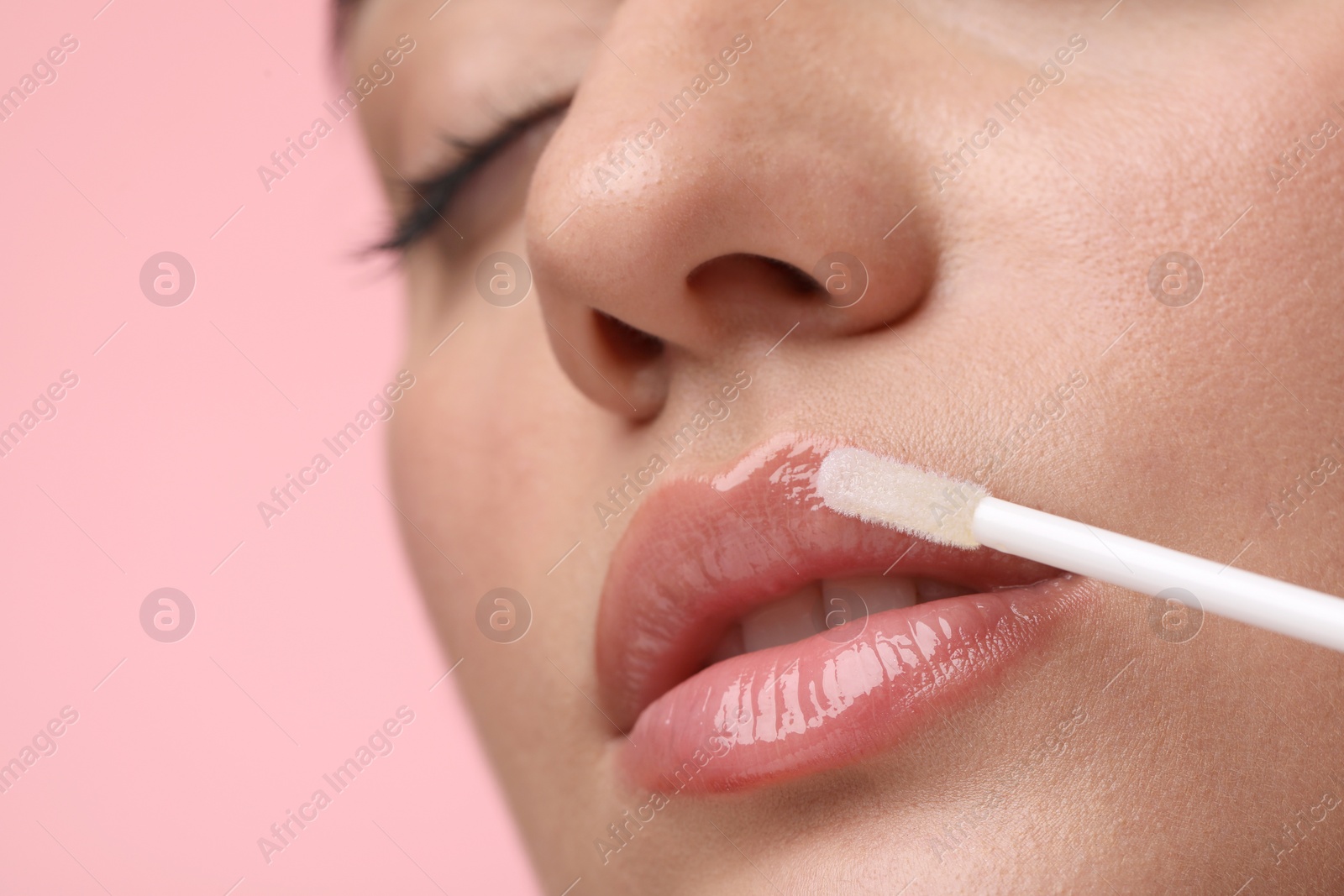 Photo of Woman applying lip gloss on pink background, closeup. Space for text