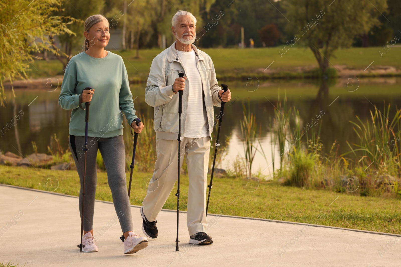 Photo of Senior man and woman performing Nordic walking outdoors, space for text