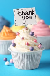Photo of Tasty cupcakes and note with phrase Thank You on light blue background