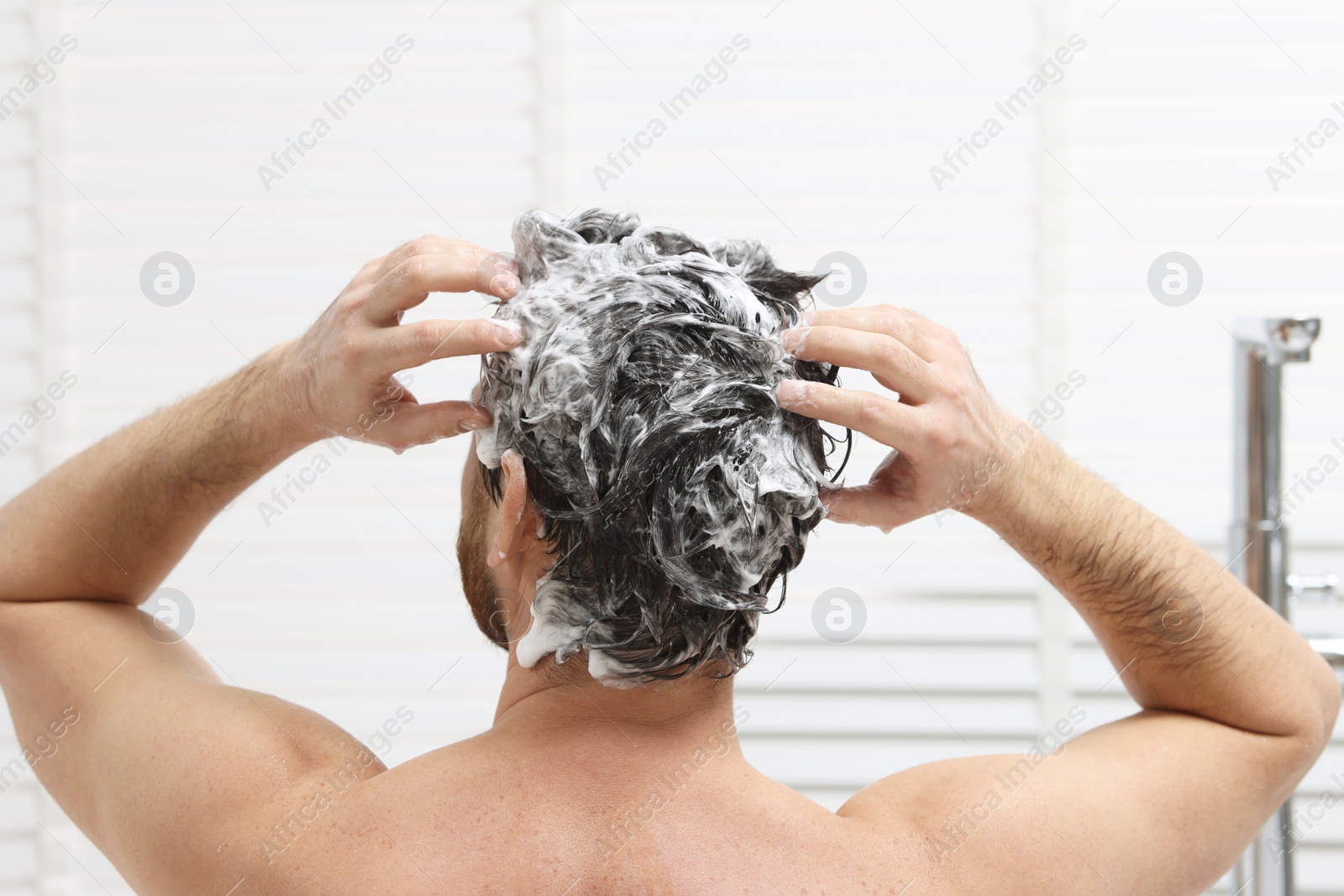 Photo of Man washing his hair with shampoo in shower, back view