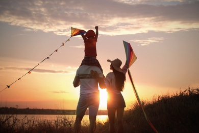 Parents and their child playing with kites outdoors at sunset, back view. Spending time in nature