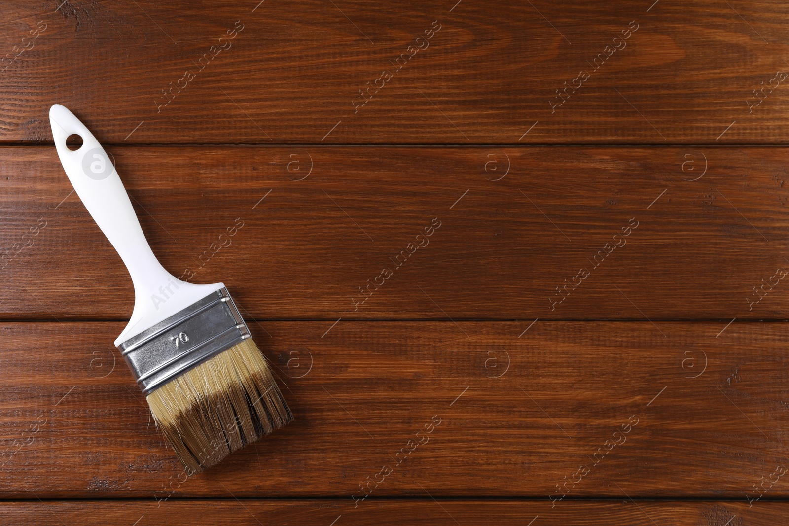 Photo of Brush with wood stain on wooden surface, top view. Space for text