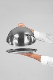 Photo of Waiter holding metal tray with lid on grey background