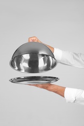 Waiter holding metal tray with lid on grey background