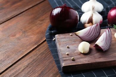Photo of Board with cut onion and garlic clove on wooden table. Space for text