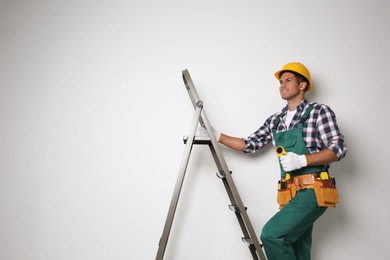 Photo of Professional builder climbing up metal ladder on light background. Space for text