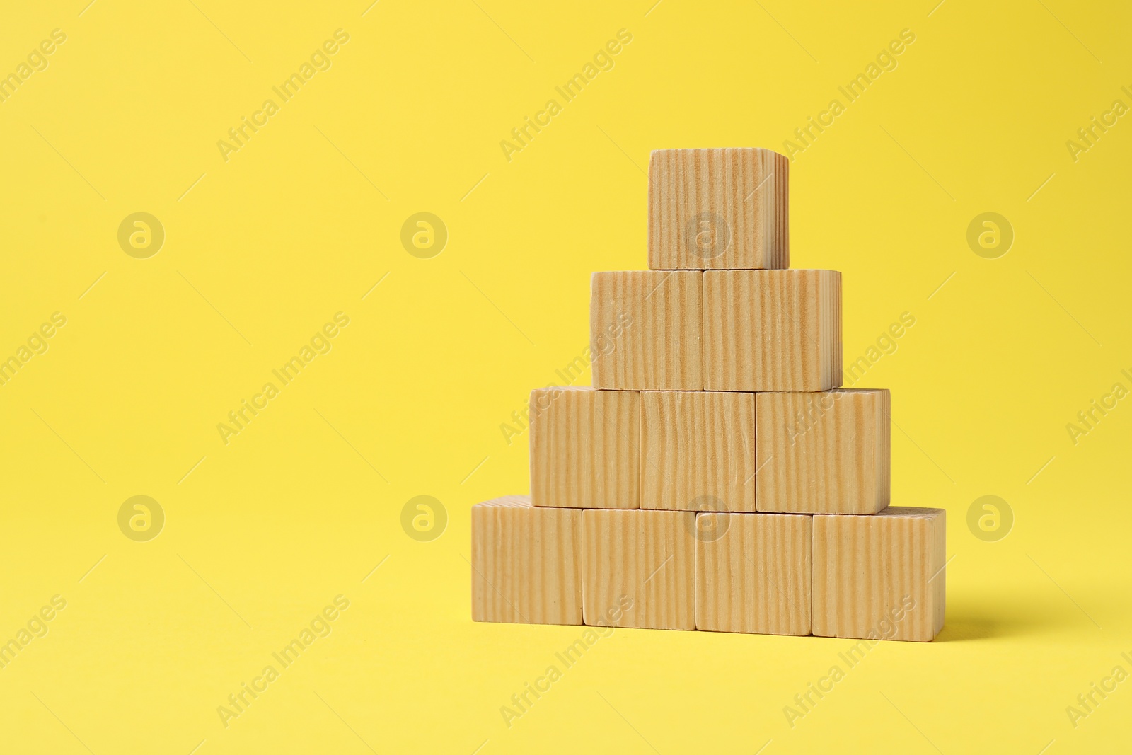 Photo of Pyramid of blank wooden cubes on yellow background, space for text