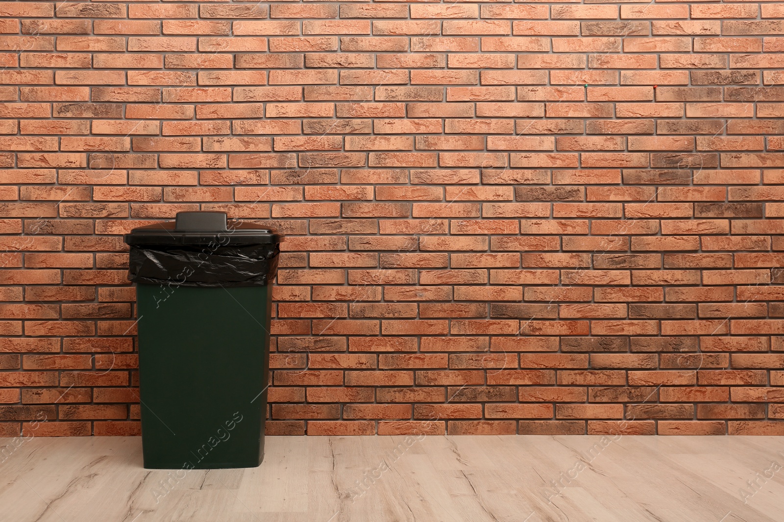 Photo of Closed trash bin near brick wall indoors, space for text. Waste recycling
