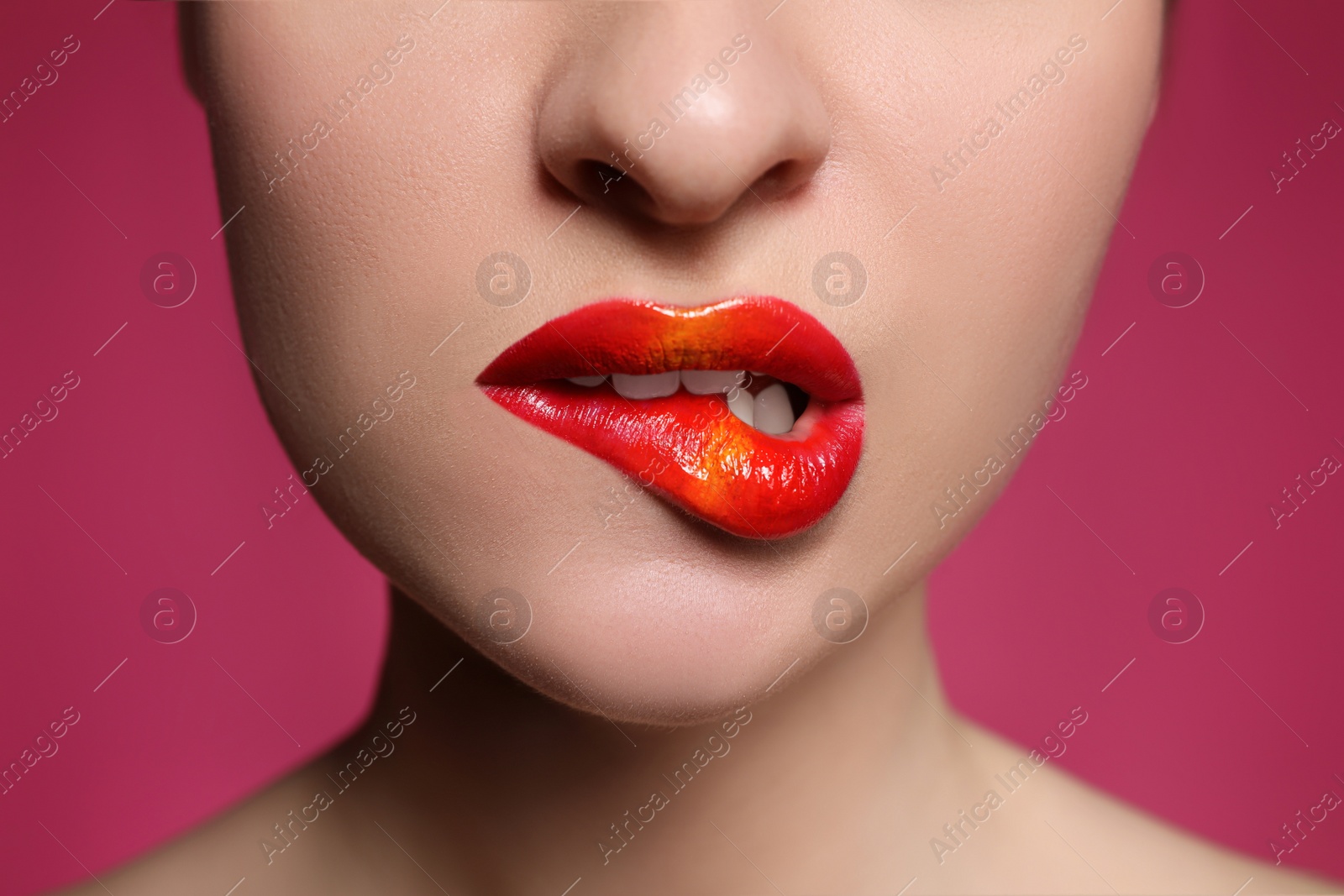 Photo of Young woman with beautiful makeup biting lip on pink background, closeup