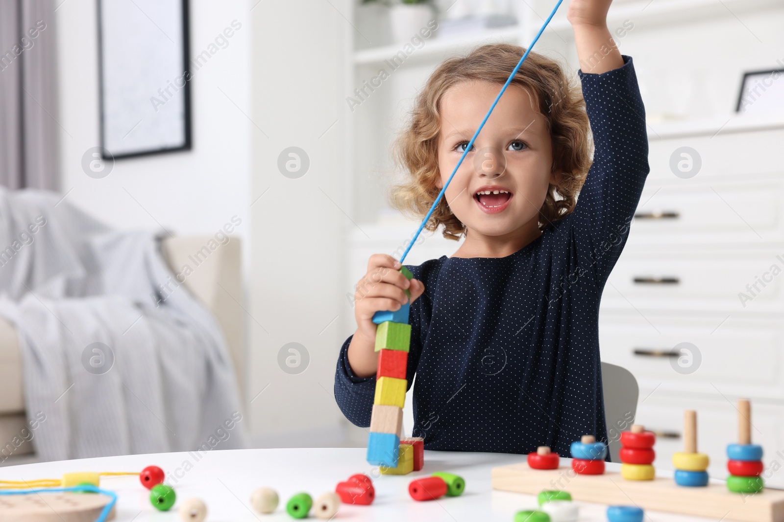 Photo of Motor skills development. Little girl playing with wooden pieces and string for threading activity at table indoors