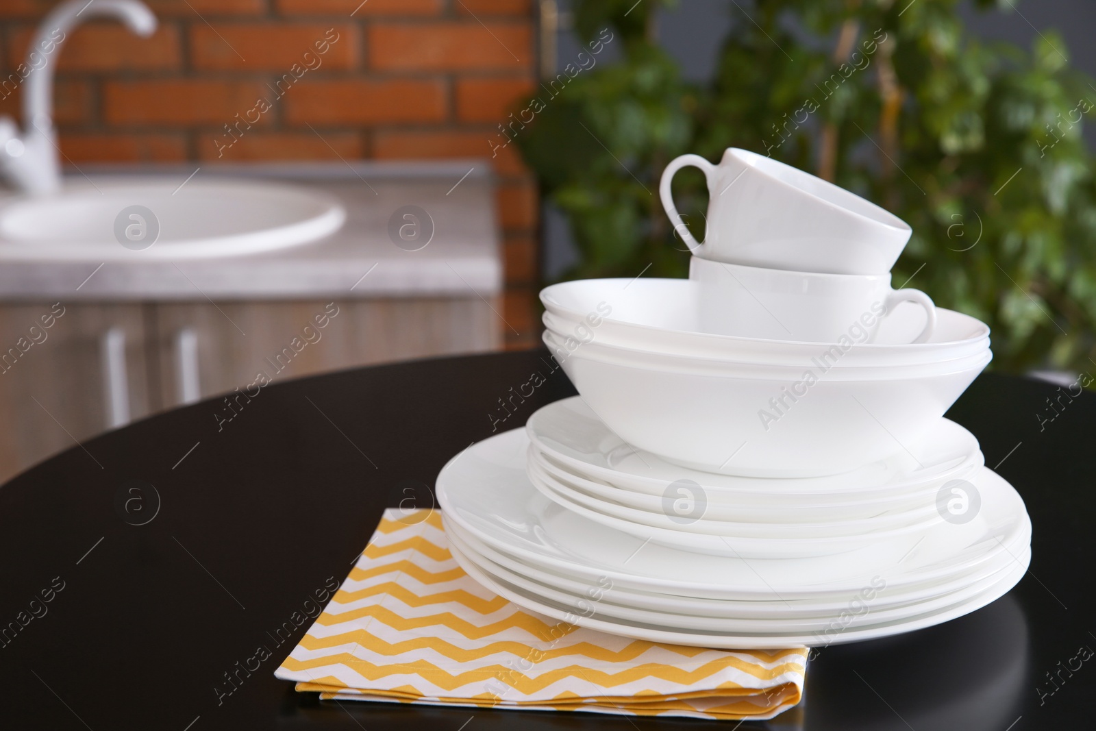 Photo of Stack of clean dishes and cups on table against blurred background. Space for text