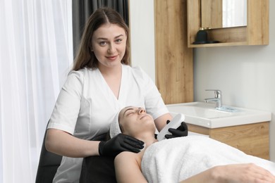 Photo of Cosmetologist using ultrasonic scrubber. Client having cleansing procedure in clinic