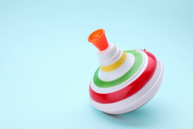 Photo of One bright spinning top on light blue background, closeup with space for text. Toy whirligig