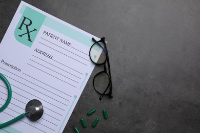 Medical prescription form, stethoscope, pills and glasses on dark grey table, flat lay. Space for text