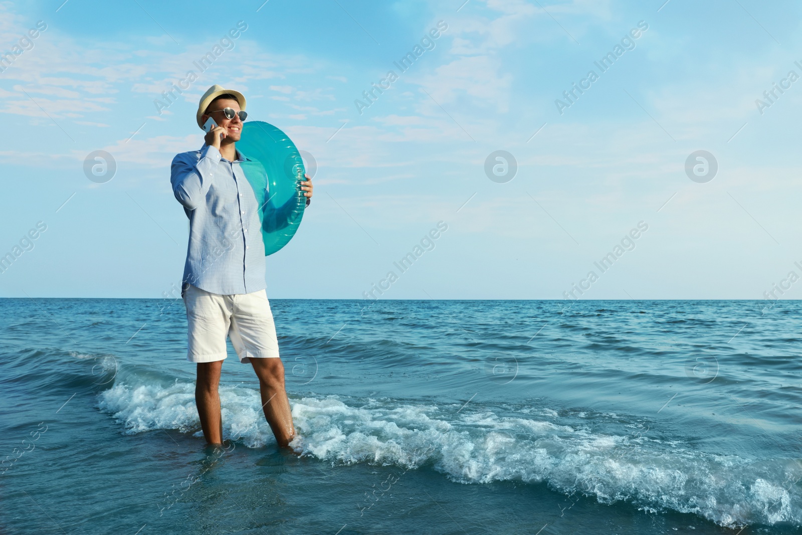 Photo of Happy man with inflatable ring talking by mobile phone near sea on beach. Business trip