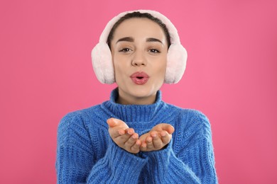 Beautiful young woman wearing earmuffs on pink background