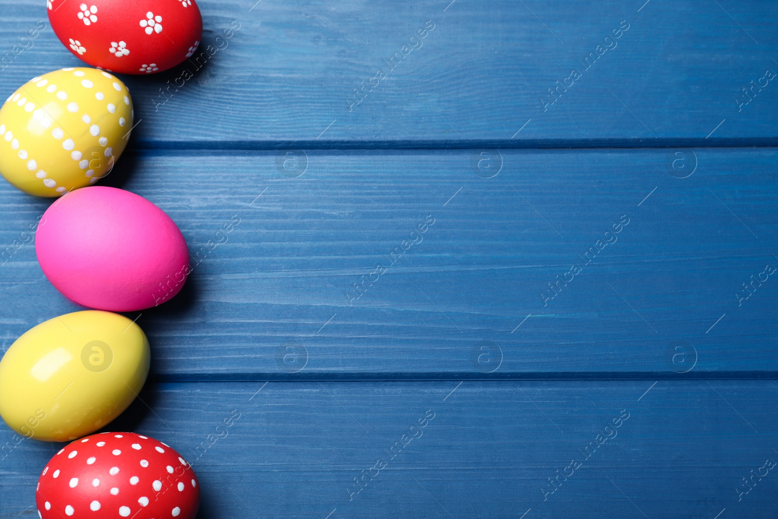 Photo of Bright painted eggs on blue wooden table, flat lay with space for text. Happy Easter