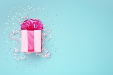 Photo of Pink gift box with confetti and streamers on light blue background, flat lay. Space for text