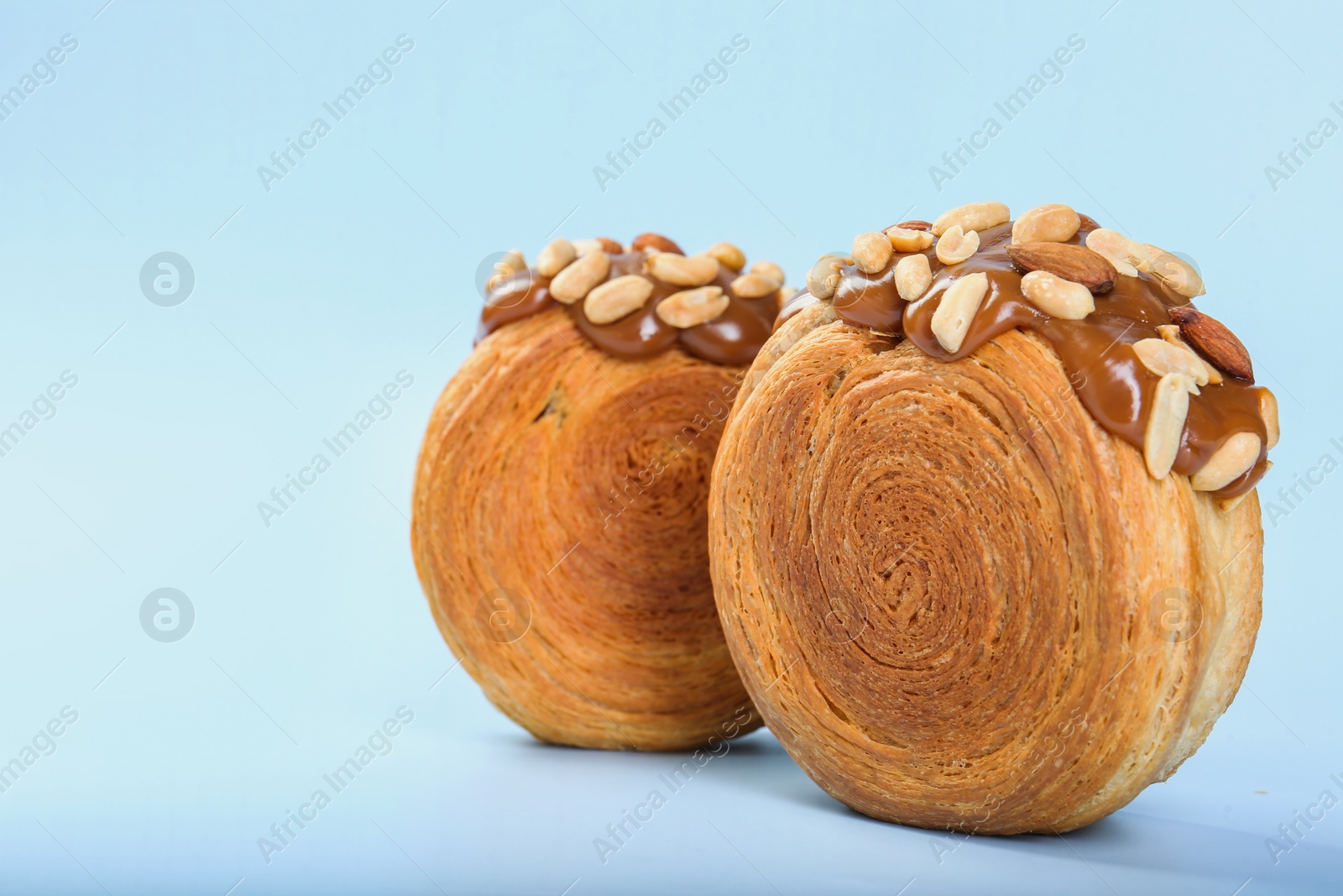 Photo of Tasty puff pastry. Supreme croissants with chocolate paste and nuts on light blue background, closeup. Space for text