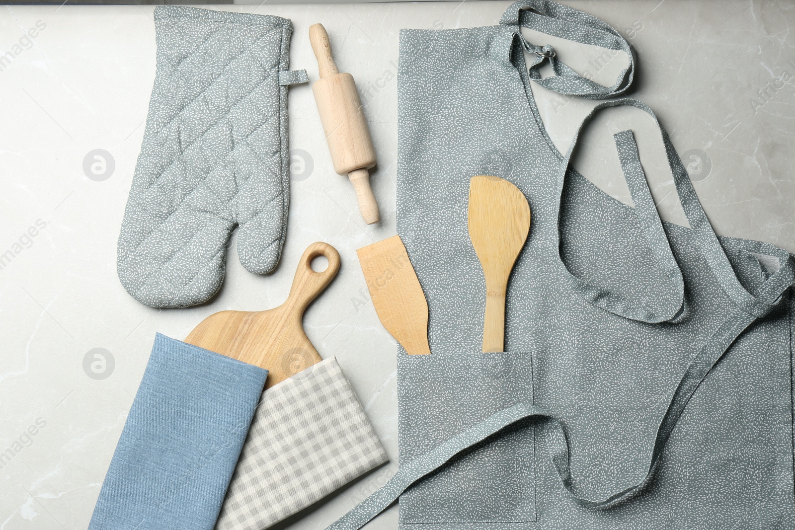 Photo of Kitchen napkins, apron and different utensils on light grey table, flat lay