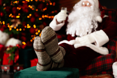 Santa Claus with glass of milk resting in armchair near Christmas tree, focus on legs