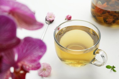 Glass cup of freshly brewed tea and flowers on light table