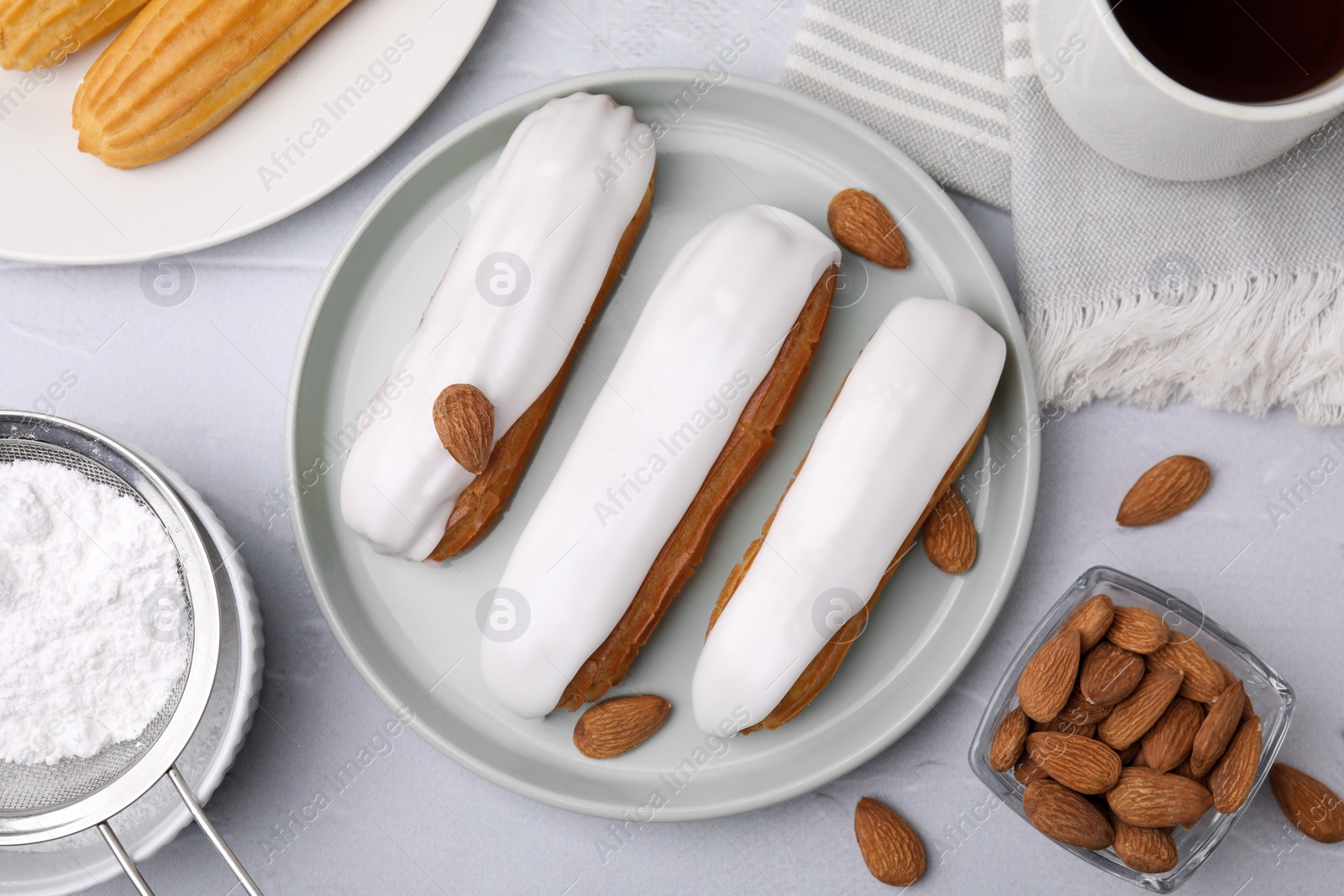 Photo of Delicious eclairs covered with glaze, flour and almonds on white textured table, flat lay
