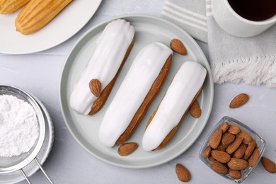 Delicious eclairs covered with glaze, flour and almonds on white textured table, flat lay