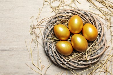 Nest with golden eggs on white wooden table, flat lay. Space for text