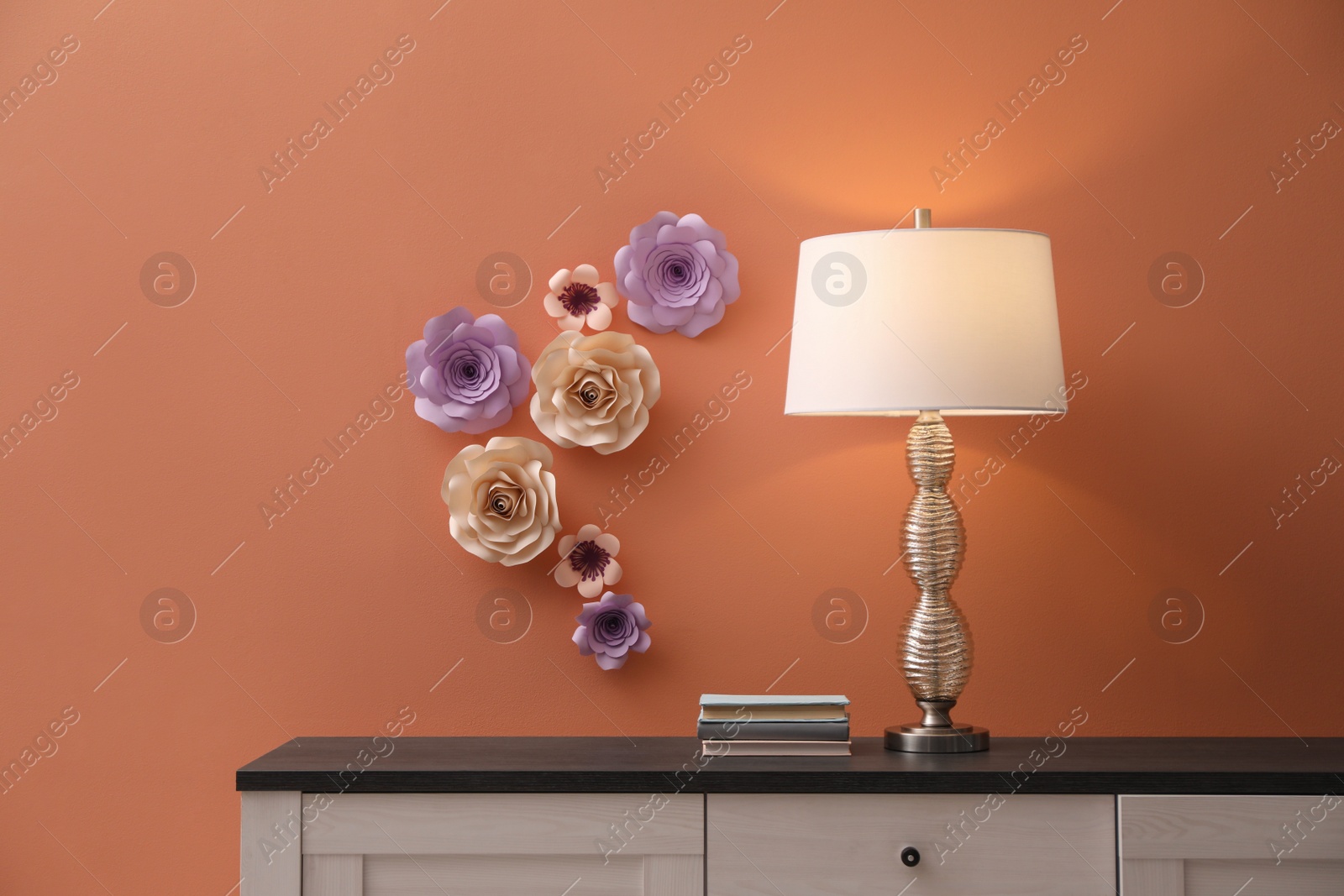 Photo of Lamp and books on cabinet near coral wall with floral decor