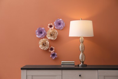 Lamp and books on cabinet near coral wall with floral decor