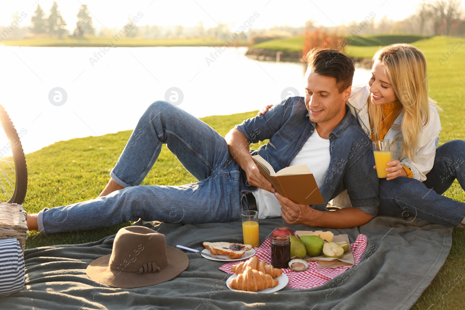 Photo of Happy young couple having picnic near lake on sunny day