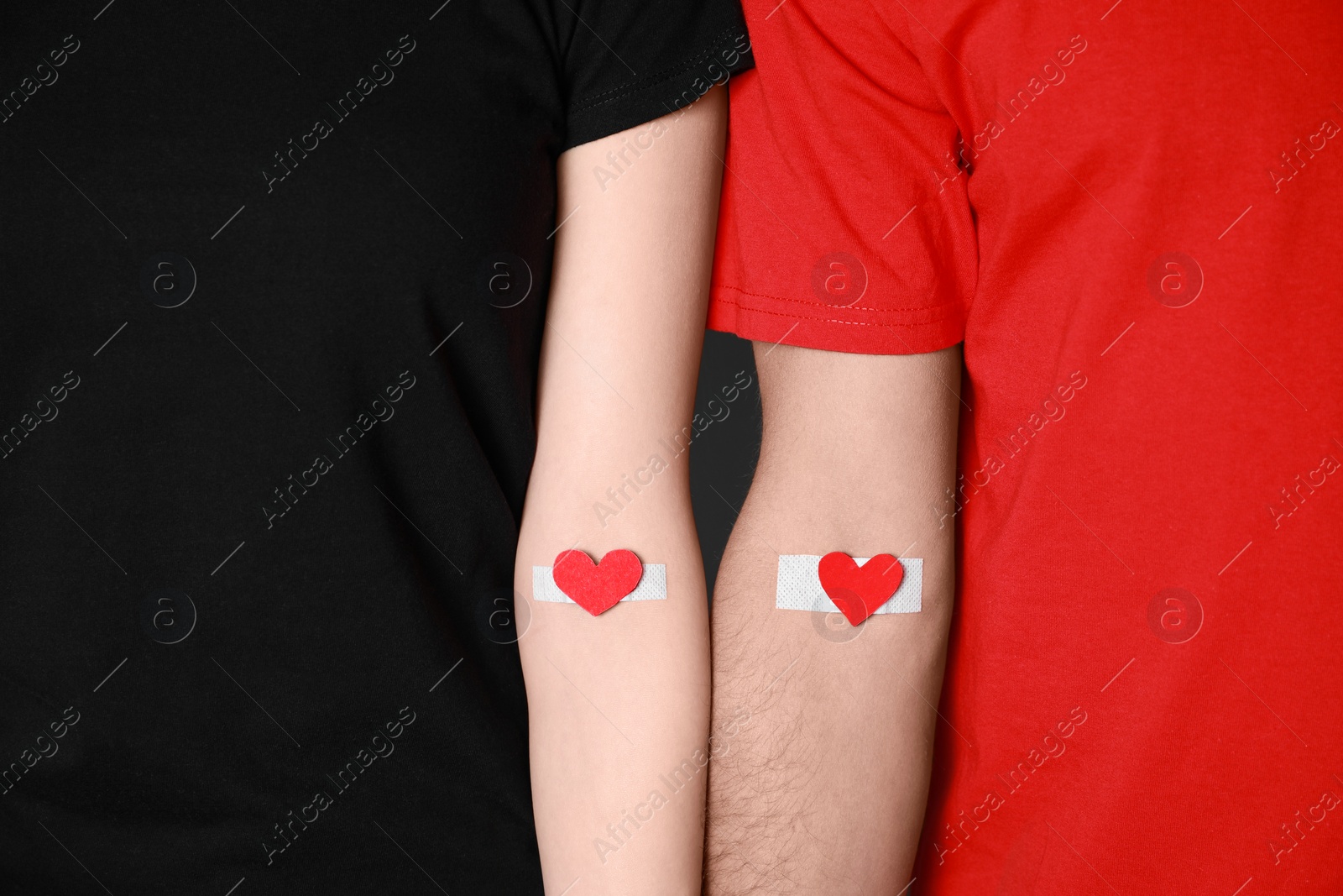 Photo of Blood donation concept. Couple with adhesive plasters on arms against grey background, closeup