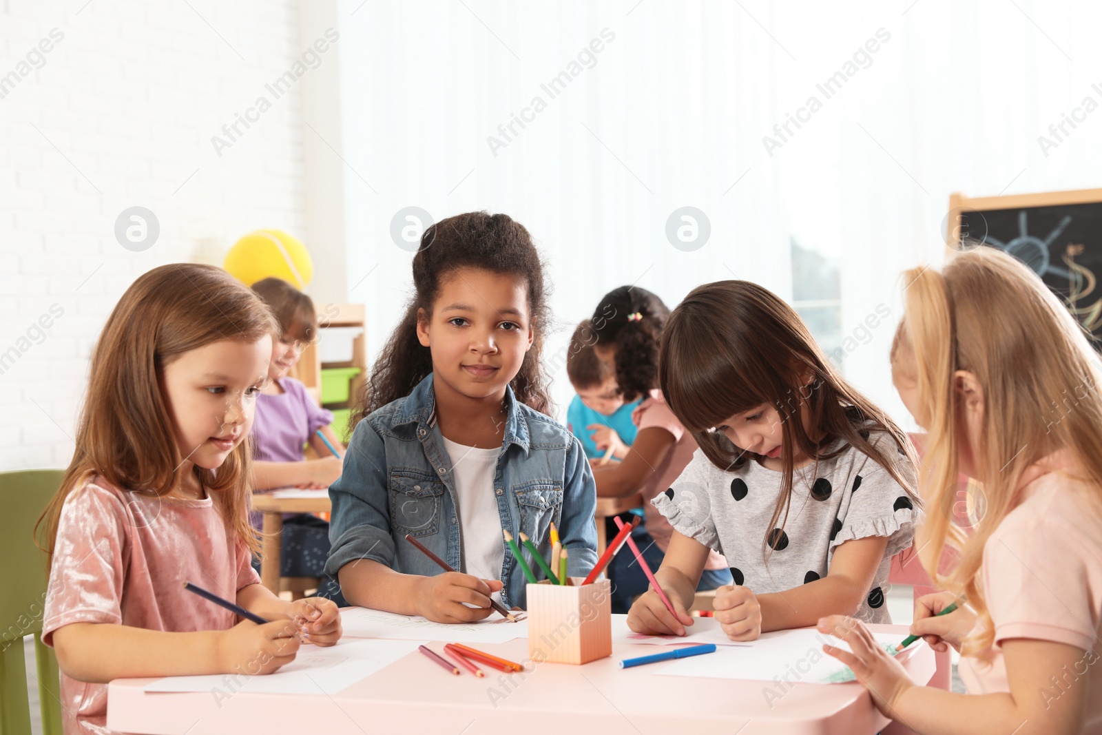 Photo of Adorable children drawing together at table indoors. Kindergarten playtime activities