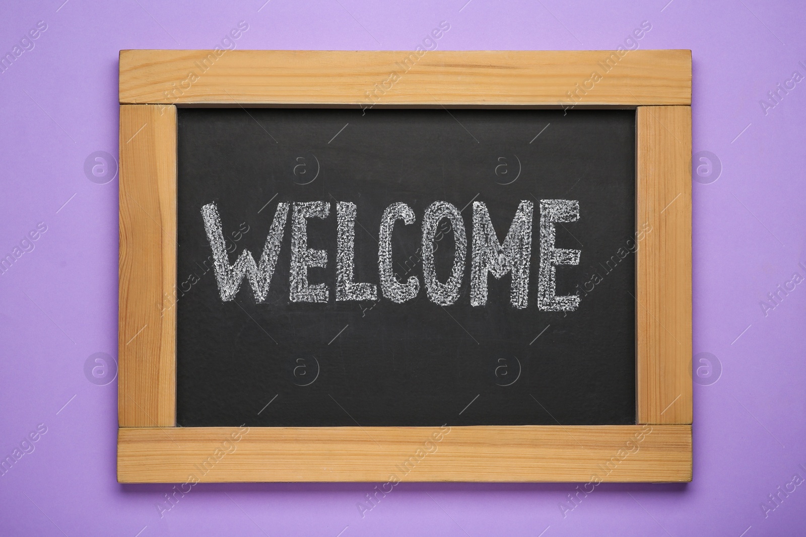 Photo of Small chalkboard with word Welcome on violet background, top view