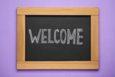 Small chalkboard with word Welcome on violet background, top view