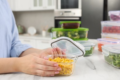 Woman sealing container with corn at white marble table in kitchen, closeup. Food storage