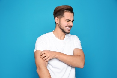 Photo of Young man scratching arm on color background. Annoying itch