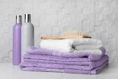 Folded towels, hair brush and shampoo on table against white wall.
